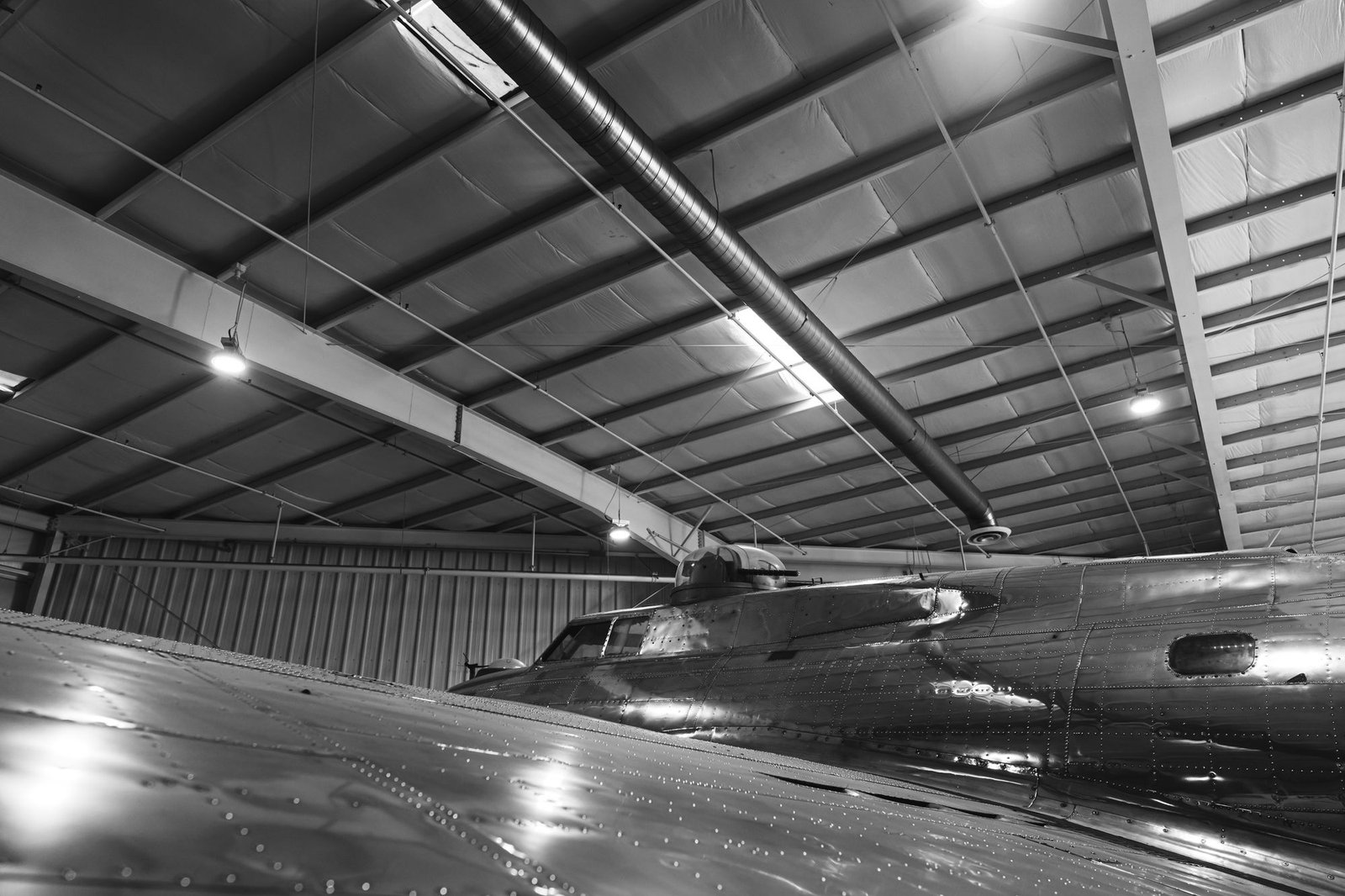 A polished aircraft fuselage reflecting the lights of a dark hangar