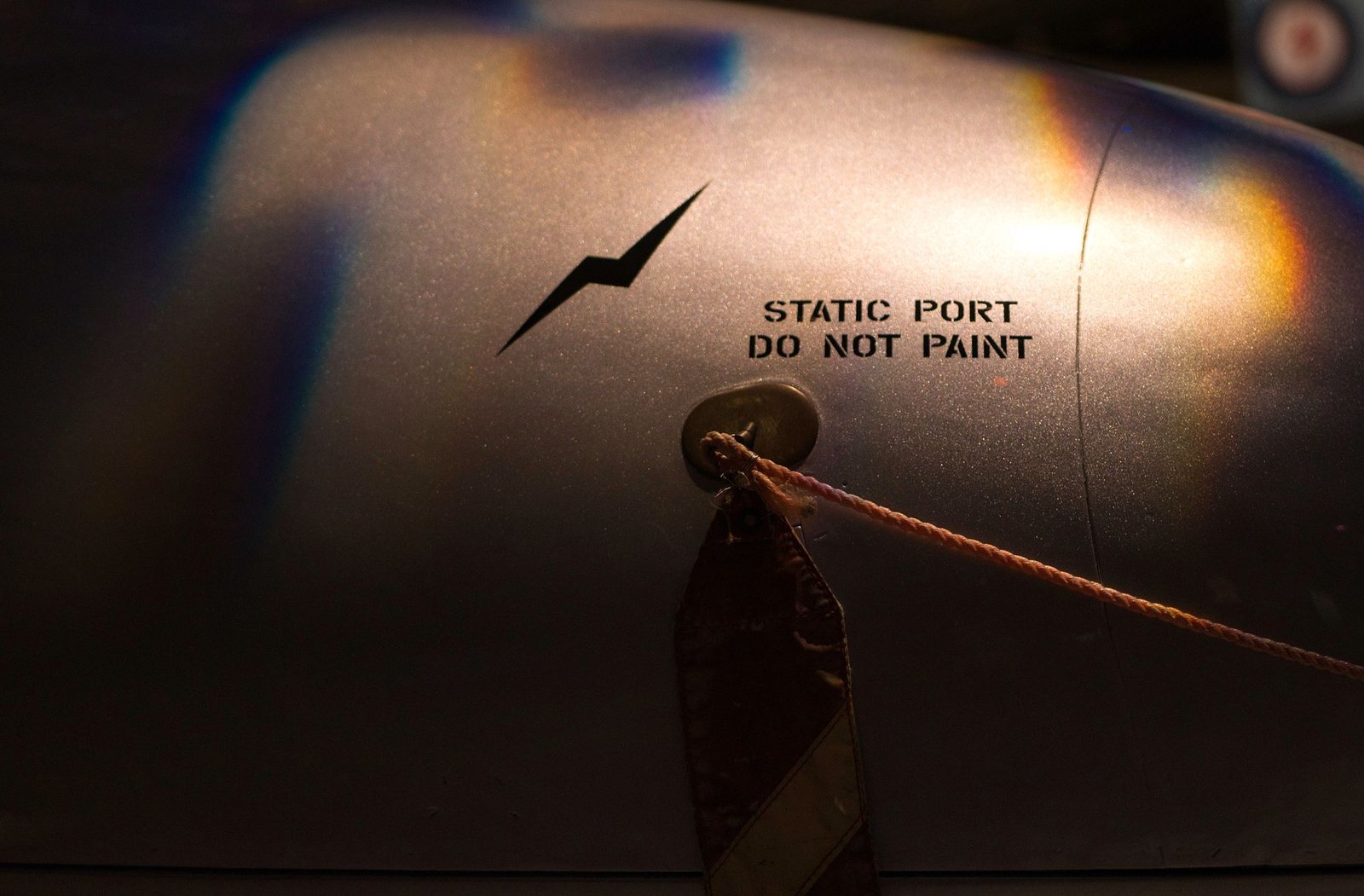 Close-up of a fuselage static port with a red remove-before-flight streamer and the stencil Static Port Do Not Paint